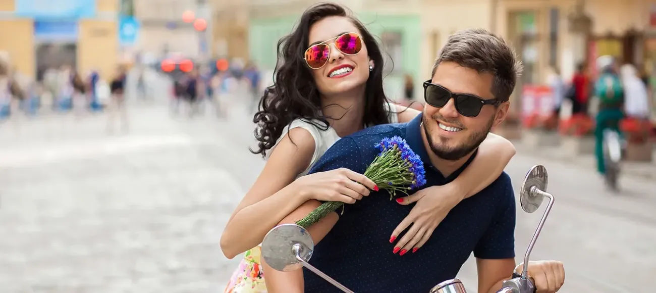 A happy couple riding a motorbike through a cobblestone street.