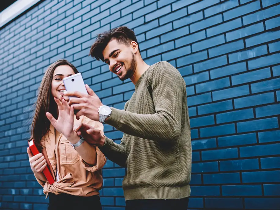 Deux personnes regardant un téléphone, devant un mur en briques bleues.