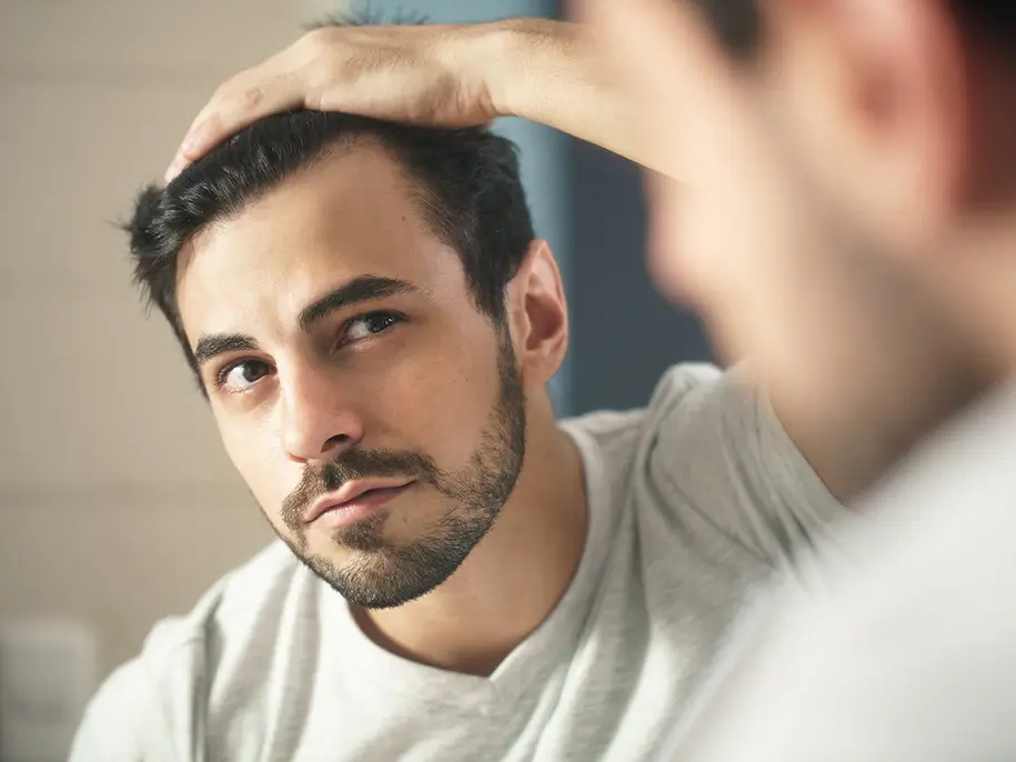 Un homme se regarde dans le miroir en passant sa main dans ses cheveux.